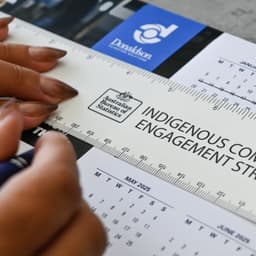 A ruler featuring a light colour with text, being held above a calendar on a table surface.