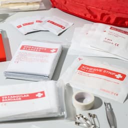 A red first aid kit containing various items, including an emergency blanket, adhesive strips, triangular bandages, and more.