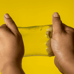 A pair of hands stretching a translucent yellow jelly cube sensory toy against a bright yellow background.