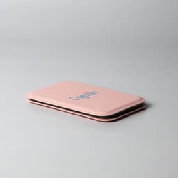 A pink pocket mirror with a slim and rectangular design, featuring a logo on the front.