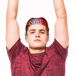 A person wearing a brightly patterned bandana, raising their arms, dressed in a red shirt. The bandana features vibrant colours.
