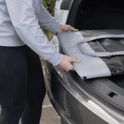 A person placing a grey and black premium foldable cooler into a car boot, showcasing its compact design.