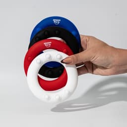 A hand holds four silicone wrist discs in red, white, blue, and black, featuring raised dots and a branding logo.