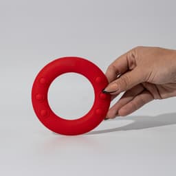 A red silicone wrist disc held in a hand, featuring textured grip spots along its edge.