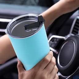 A drink bottle in teal, featuring a double wall design and a black straw, held in a hand inside a vehicle.