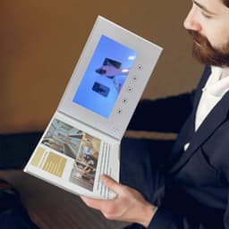 A white 7-inch LCD video brochure with an open cover displaying a video on the screen, held by a man in formal attire.