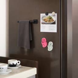 Paw shape clog shoe fridge magnets in pink and white, displayed on a dark fridge alongside a towel and an image.