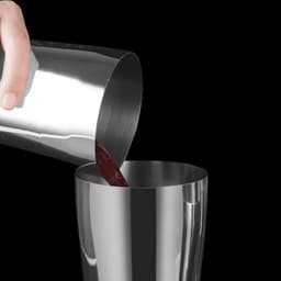 A stainless steel cocktail shaker with a sleek silver finish, pouring liquid into a glass.