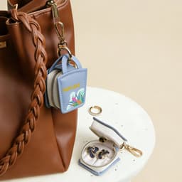 A mini blue PU leather jewellery box, open to reveal jewellery, attached to a brown bag. Features a logo.