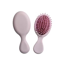 A mini paddle brush in soft pink with a textured grip and flexible bristles. It features a simple logo on the handle.