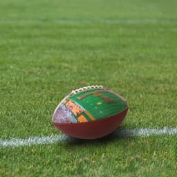 A promotional American football featuring a field design, placed on green grass with white lines. It has a logo.