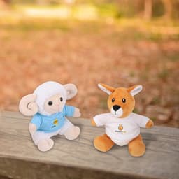 Two plush toys: a sheep in a blue shirt and a kangaroo in a white shirt, both with branding, set in a natural outdoor setting.