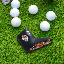 A black custom blade putter cover with colourful designs, surrounded by six white golf balls on grass.