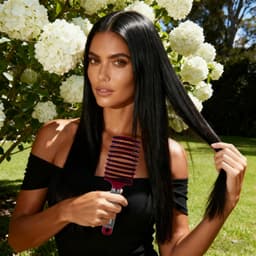 A detangler bristle hairbrush with a pink handle, held by a woman with long, straight black hair, surrounded by white flowers.