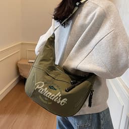 A Dumpling Crossbody Bag in olive green with a logo, worn over a grey sweatshirt, against a light background.