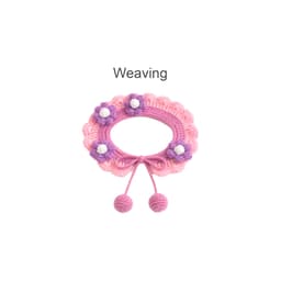 A pink crochet pet bib features scalloped edges, purple and white flower embellishments, and tied ends with pom-poms.