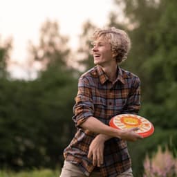 A young person throwing a colourful PU Soft Frisbee with a lion design, surrounded by greenery.