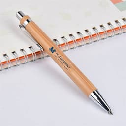 A bamboo pen with a silver clip rests on a lined notebook, featuring a logo on its barrel.