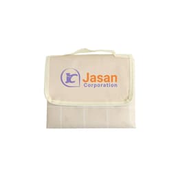 A cream picnic blanket with a green trim and a logo on the front, folded and secured with a handle.