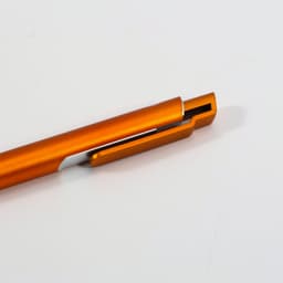 An orange ballpoint pen with a sleek design and a clip. It has a metallic finish and a logo on its body.