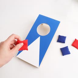 A mini cornhole game board in blue and white, with red and blue bean bags beside it.