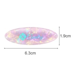 An oval iridescent hair clip in shades of pink and purple, featuring a logo, measuring 6.3cm by 1.9cm.