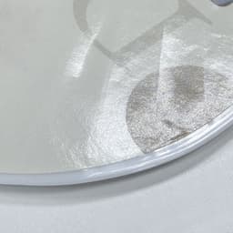 A circular, glossy PVC hand fan featuring a subtle design and clear, flexible edges. It has a light, neutral colour.