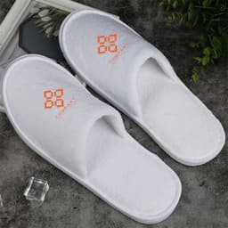 White hotel slippers with a logo on the upper side, featuring a soft texture and a simple design.