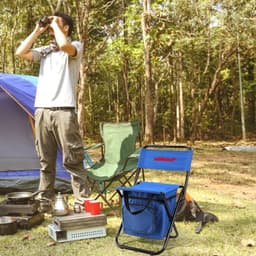 A blue foldable camping chair with a cooler bag attached, set in a campsite with tents and a person using binoculars.