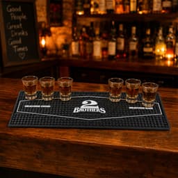 A black moulded PVC bar runner with five shot glasses arranged on it, set against a wooden bar backdrop.