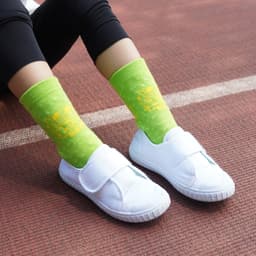 Bright green football socks with a towel bottom, worn with white slip-on shoes, against a textured surface.
