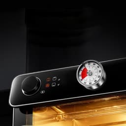 A kitchen appliance with a sleek black panel, featuring a dial and a round temperature gauge.