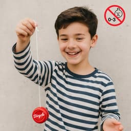 A wooden yoyo in vibrant red, held by a smiling child wearing a striped shirt, with a logo visible.