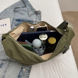 An olive green crossbody bag opened to display various items, including a drink bottle, a notebook, and makeup products.