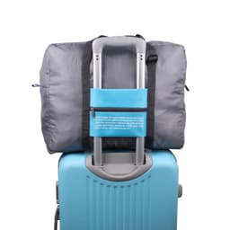A grey travel compressed bag attached to the handle of a blue suitcase. The bag features a pocket and a logo.