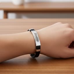 A black leather bracelet with a silver metal plate and a logo, resting on a wooden surface.