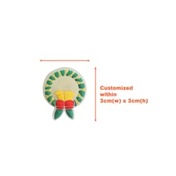 A circular shoe charm in yellow, green, and red, featuring a floral design, with a logo.