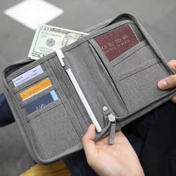 A grey passport holder with compartments for cards, cash, and a boarding pass, held open by a person.