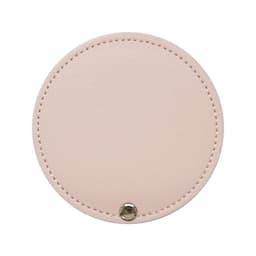 A round makeup mirror in a soft pink colour with a stitched edge and a metal button detail.