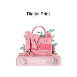A pink 3D paper art handbag notepad, embellished with flowers and a bow, resting on a flat base with a logo.