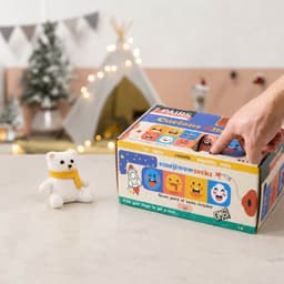 A colourful multi-compartment box with various playful emoji designs and a small white teddy bear beside it.