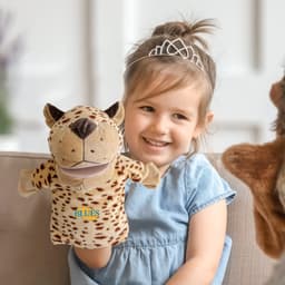 A plush leopard hand puppet in shades of brown and cream, held by a young girl, sitting on a couch.