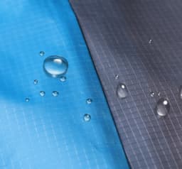 A close-up of a large picnic blanket featuring blue and grey sections with water droplets on the surface.