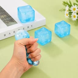 A blue squishy stress relief snowflake cube is being squeezed by a hand, with two more cubes in the background.