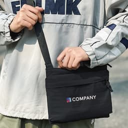 A black lightweight crossbody bag with an adjustable strap and a logo on the front, being held by a person.