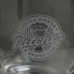 A glass featuring a logo for a grill house and sport bar, presented in clear glass with a decorative design.