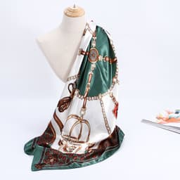A silk satin scarf in green and white with decorative patterns and a logo, displayed on a mannequin.