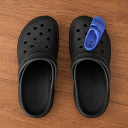 A pair of black clog shoes with a single blue charm positioned on one of the shoes.