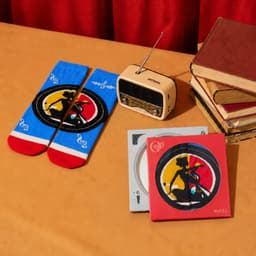 A red and blue pair of socks, a vintage radio, and two CDs in decorative cases on a table with books.