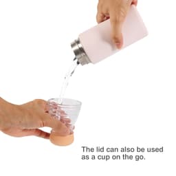 A drink bottle in soft pink, pouring liquid into a clear cup. It has a stainless steel lid that doubles as a cup.